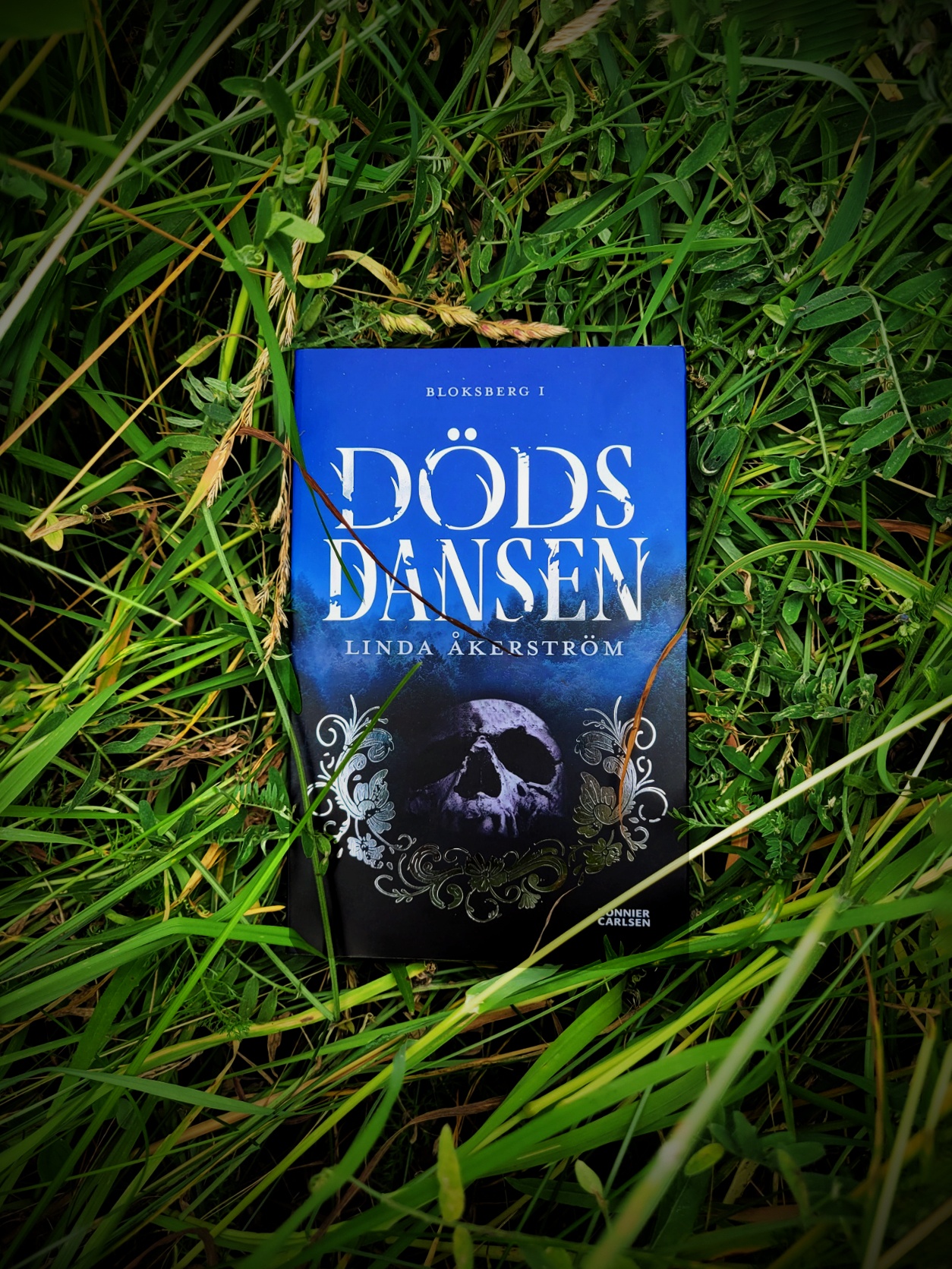Boken Dödsdansen av Linda Åkerström som ligger i gräset.